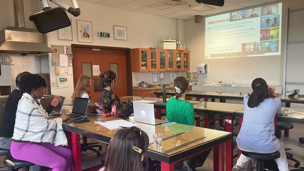 Eine Gruppe von Menschen sitzt in einem Klassenzimmer und verfolgt eine Präsentation.